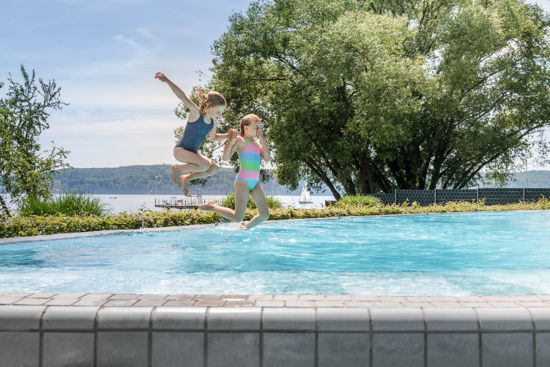 Zwei Mädchen springen gemeinsam ins Außenbecken der Bodensee-Therme Überlingen mit Blick auf den Bodensee