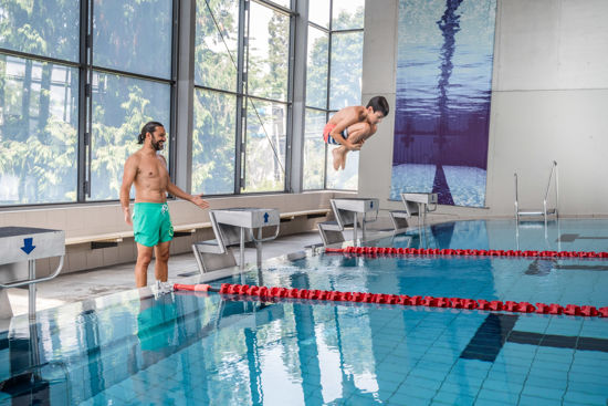 Junge springt ins Schwimmbecken der Bodensee-Therme Überlingen während ein Erwachsener am Beckenrand zusieht